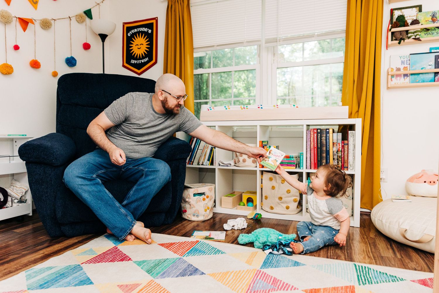 Father and daughter sitting together in their nursery passing a book to each other