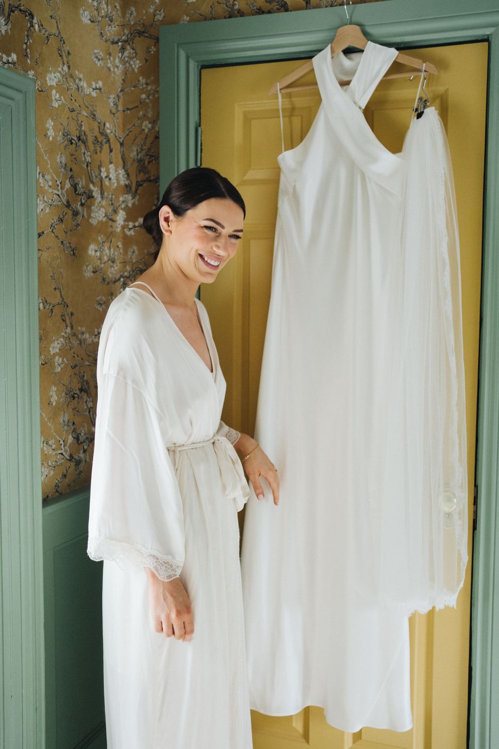 White wedding dress hanging on door frame next to person in white robe.
