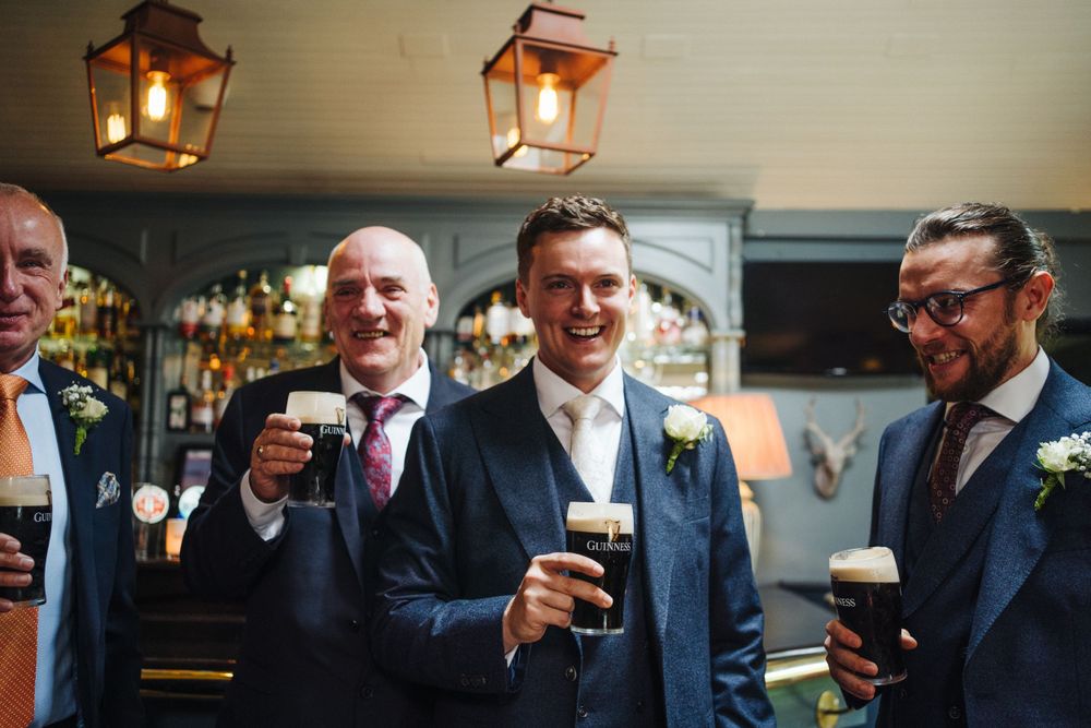 Wedding party enjoying pints of dark beer under rustic lantern lights.