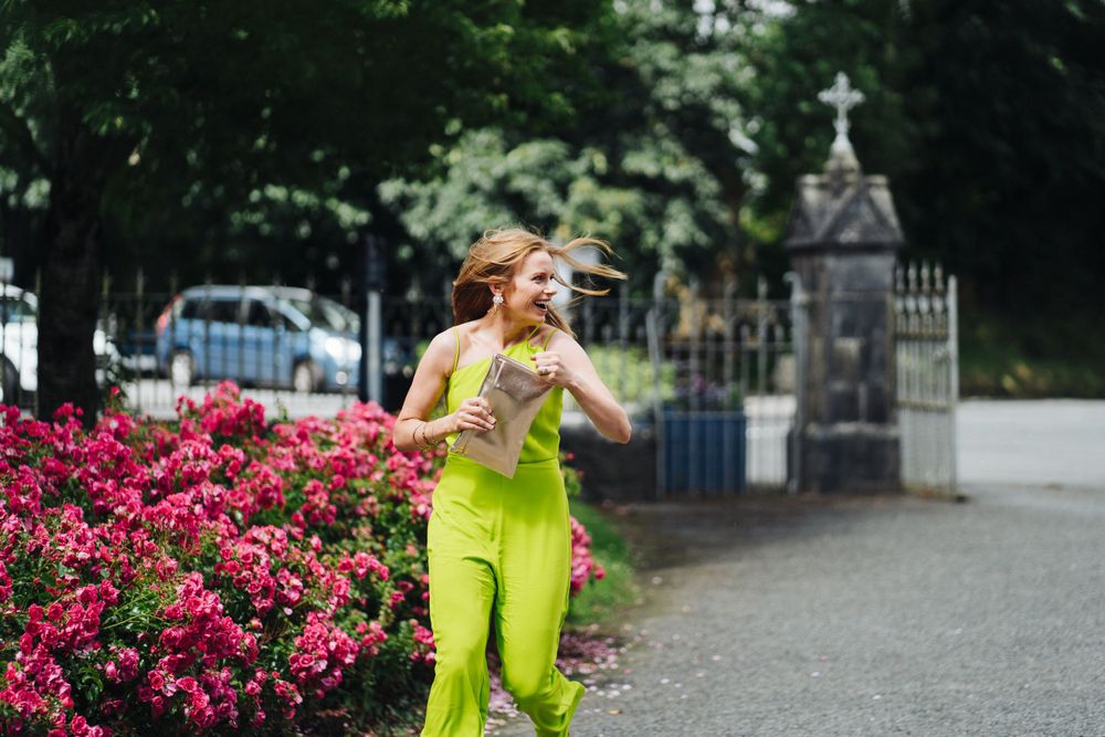 Person in bright yellow outfit running joyfully past pink flowers and iron gates.