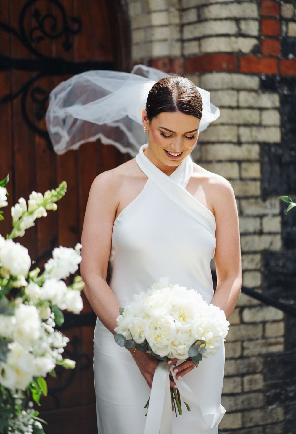 Modern bride in halter wedding jumpsuit holding white peony bouquet.