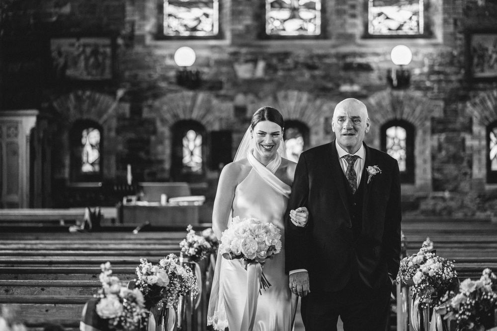 Black and white photo of a wedding ceremony in a traditional stone church with decorated aisles.