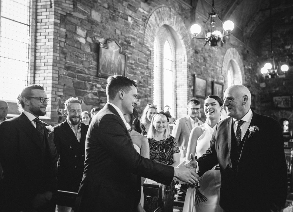 Vintage-style black and white photo of a wedding ceremony inside a stone church with arched windows.