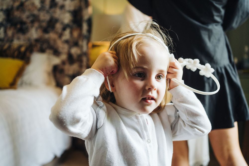 Young child in white sweater touching headphones while sitting on couch.