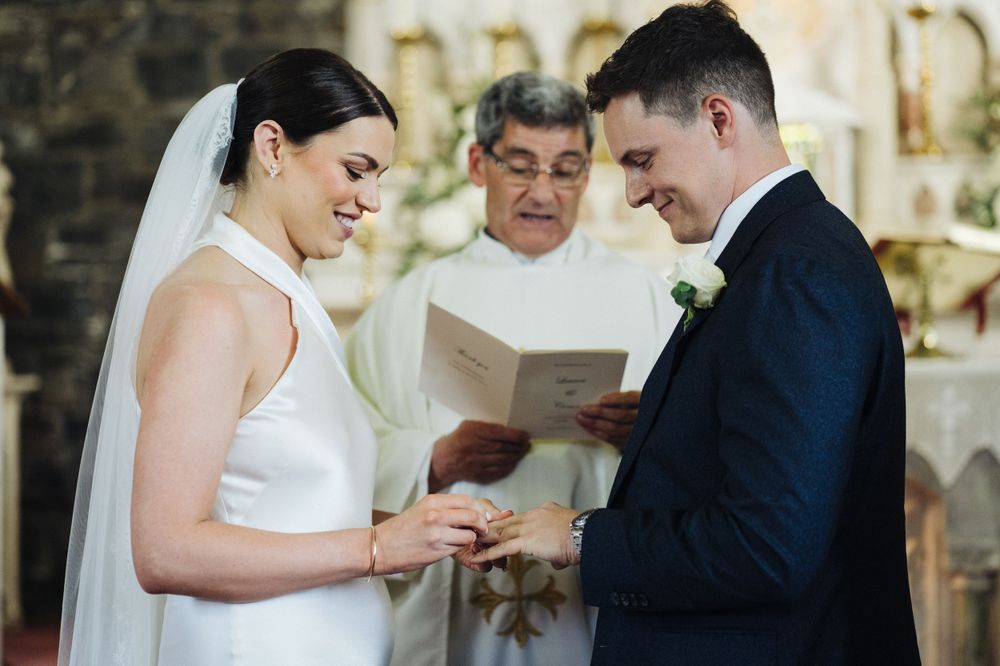 A wedding ceremony exchange of vows at the altar with officiant reading from book.