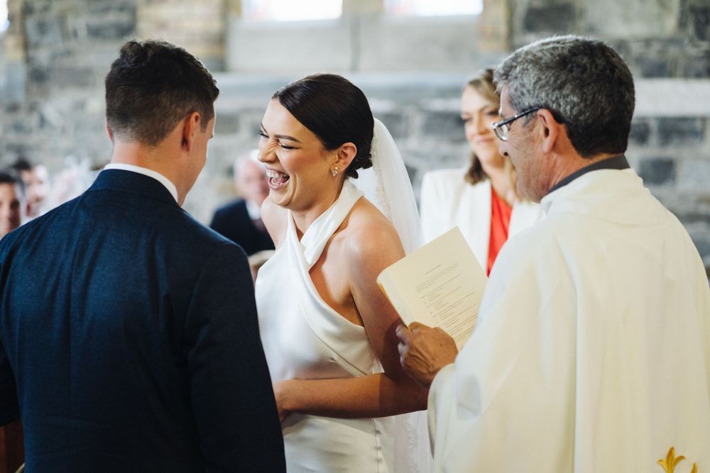 Joyful moment during wedding ceremony with couple and officiant sharing laughter at the altar.