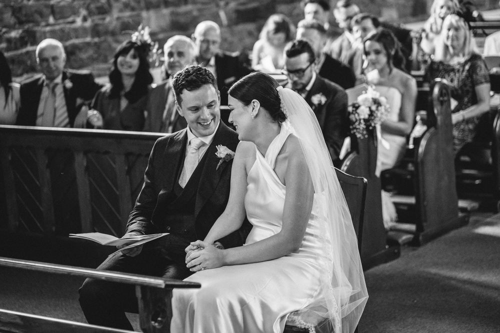 Black and white photo of couple seated in church pews during wedding ceremony.
