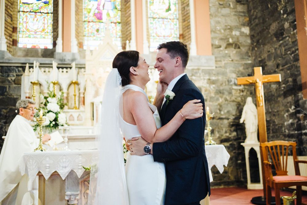 Newlyweds share an intimate moment at the altar in a historic stone church with stained glass windows.