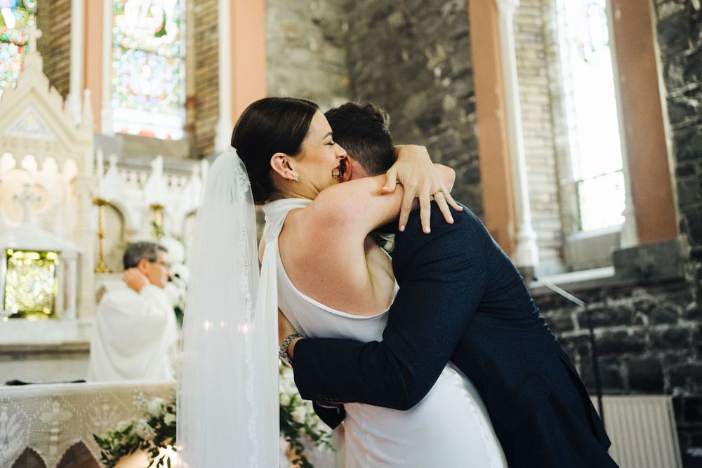 A romantic embrace during a wedding ceremony inside a traditional church with stone walls.