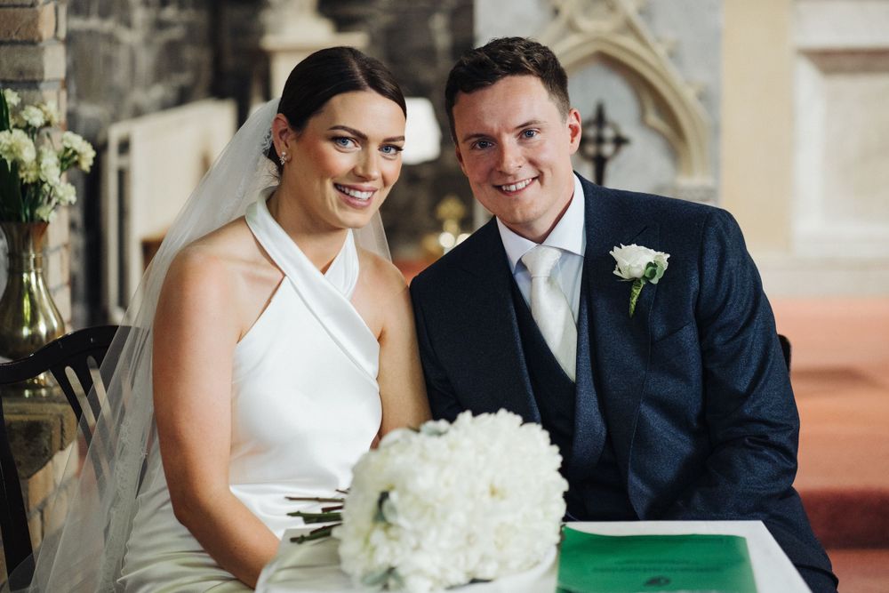 A wedding couple stands together in an elegant church interior with white floral decor.