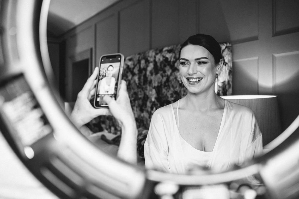 Black and white reflection of bride getting ready in circular mirror.