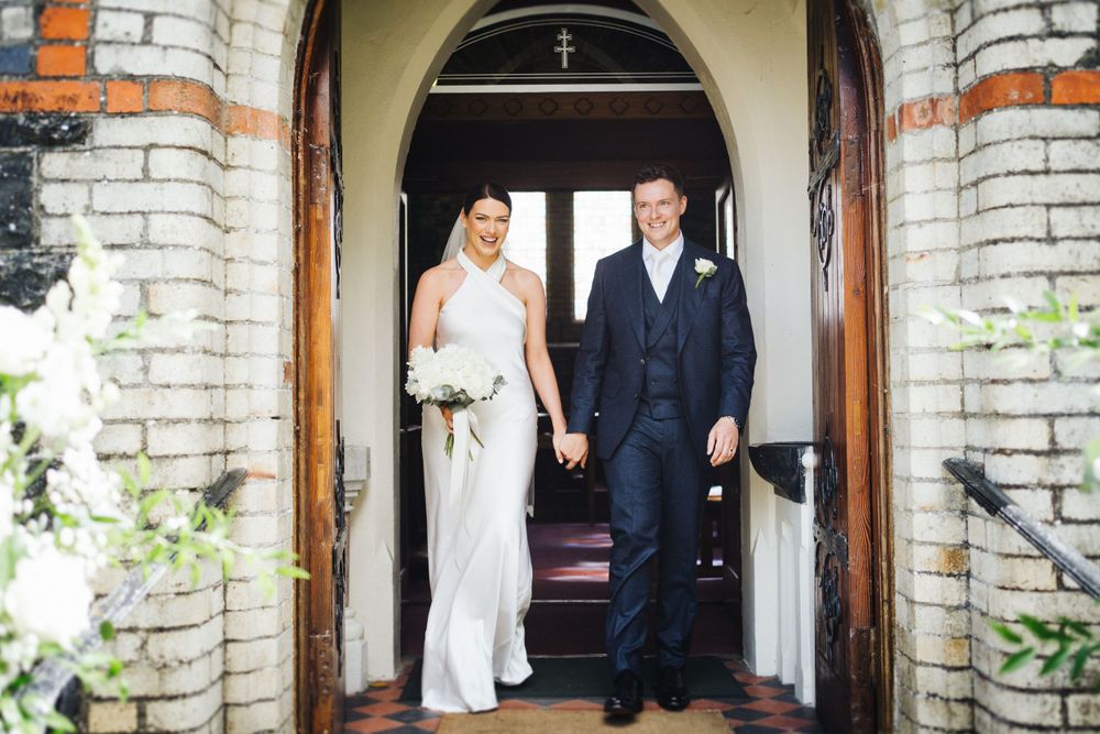A couple exits through stone archway doors at their church wedding.