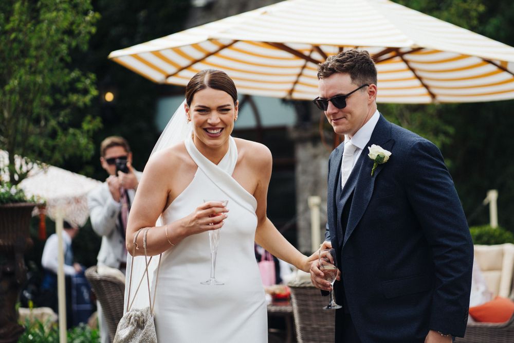 Newlyweds share a joyful moment under a striped umbrella at outdoor reception.