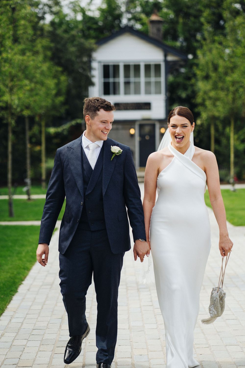 Happy couple walks hand in hand on stone pathway with white building behind them.