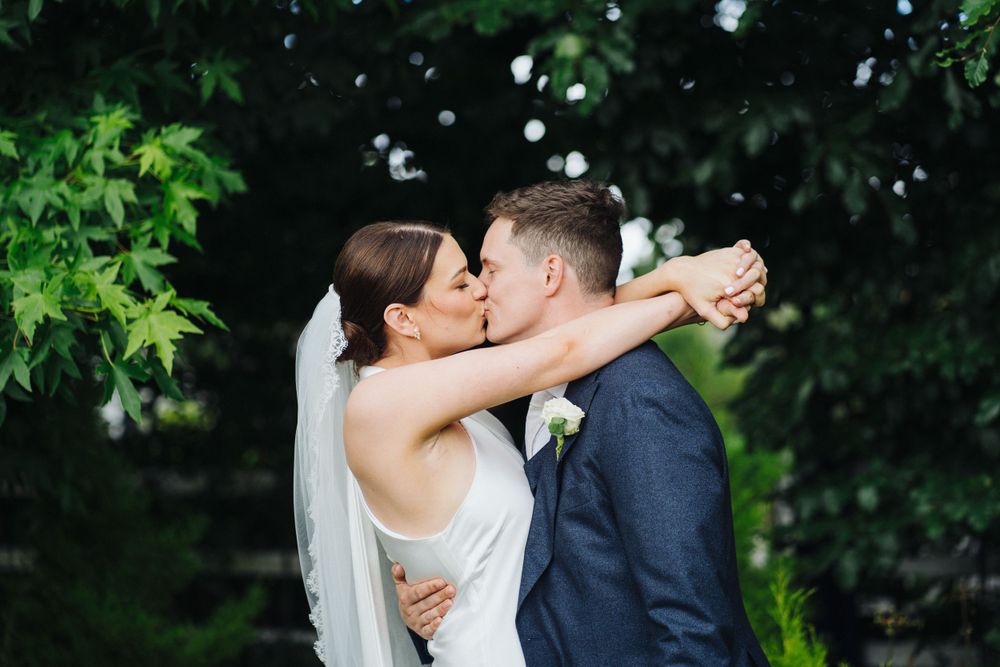 A romantic outdoor wedding kiss with the bride and groom against lush greenery.