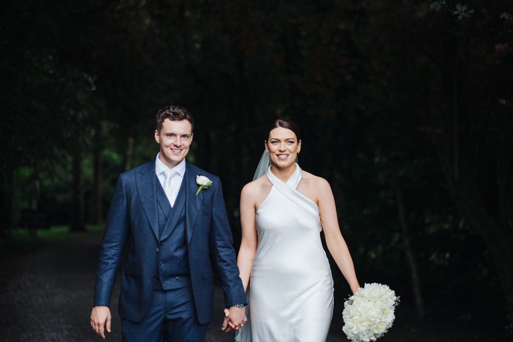 Happy couple in wedding attire smiling while walking along a garden path.