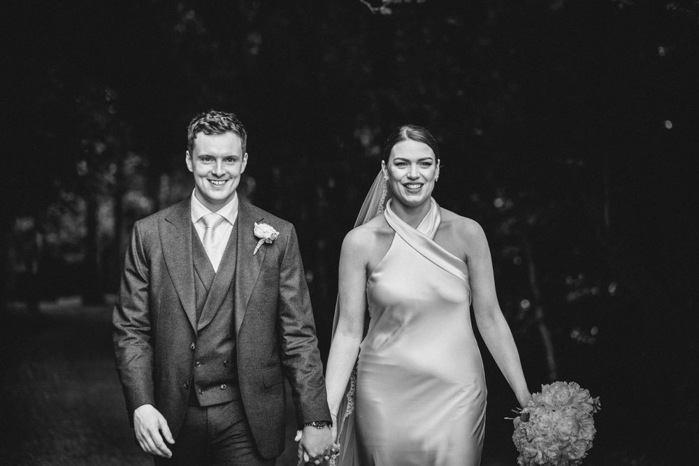 Black and white portrait of a wedding couple walking together outdoors.