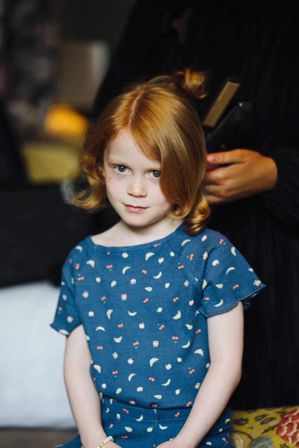 A young child in a blue polka dot dress gets their hair styled.
