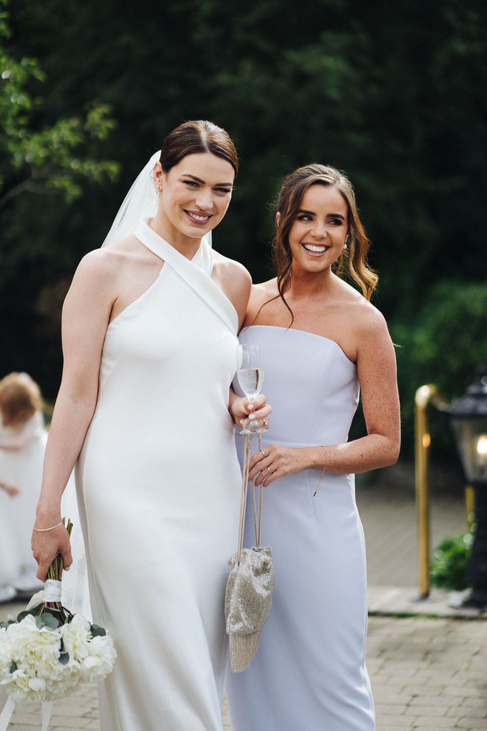 Wedding party members in elegant white and lavender dresses pose together outdoors.