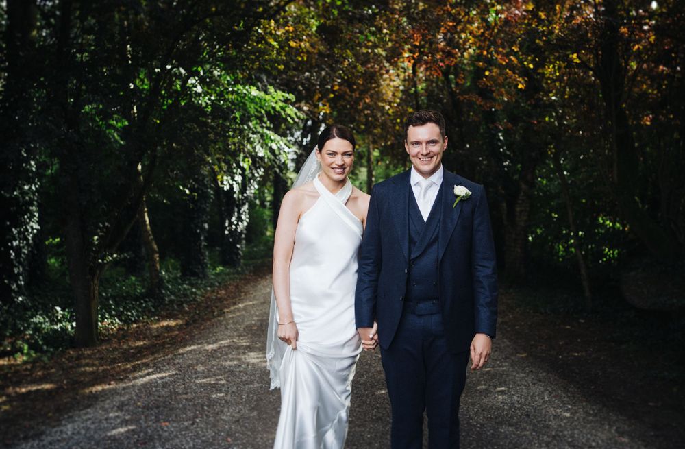 Elegant couple in wedding attire pose on a tree-lined pathway.