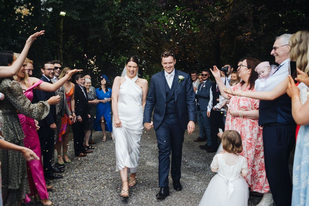 Guests line pathway to celebrate newlyweds walking through confetti shower.