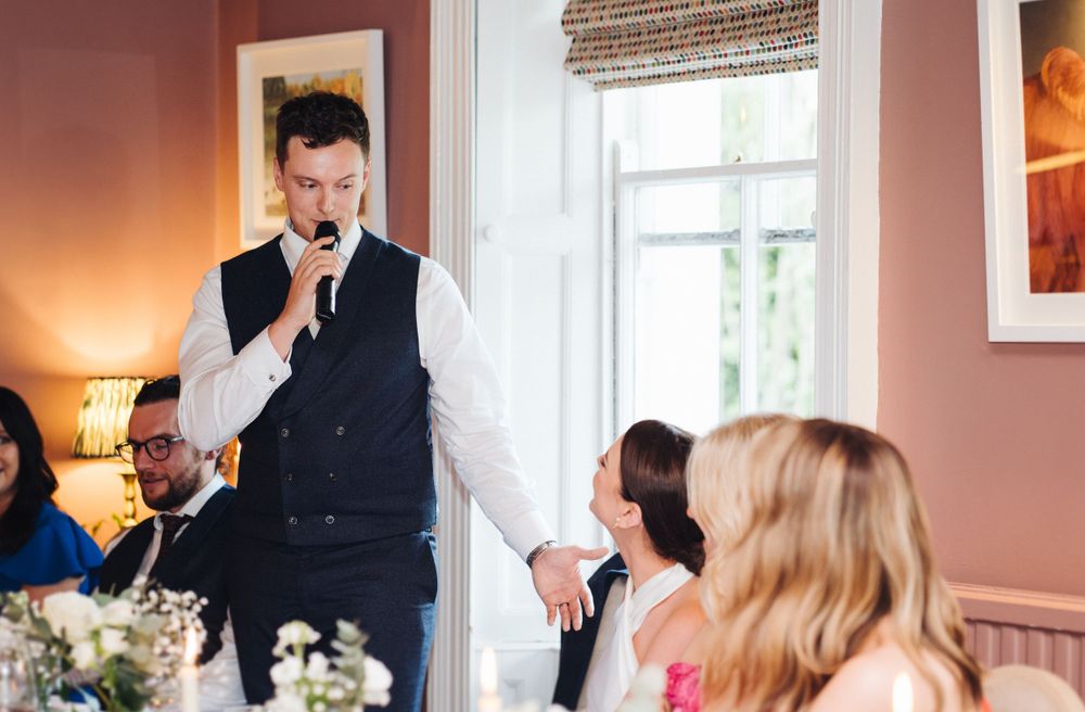Someone delivers a wedding speech in a formal vest at an elegant indoor reception.