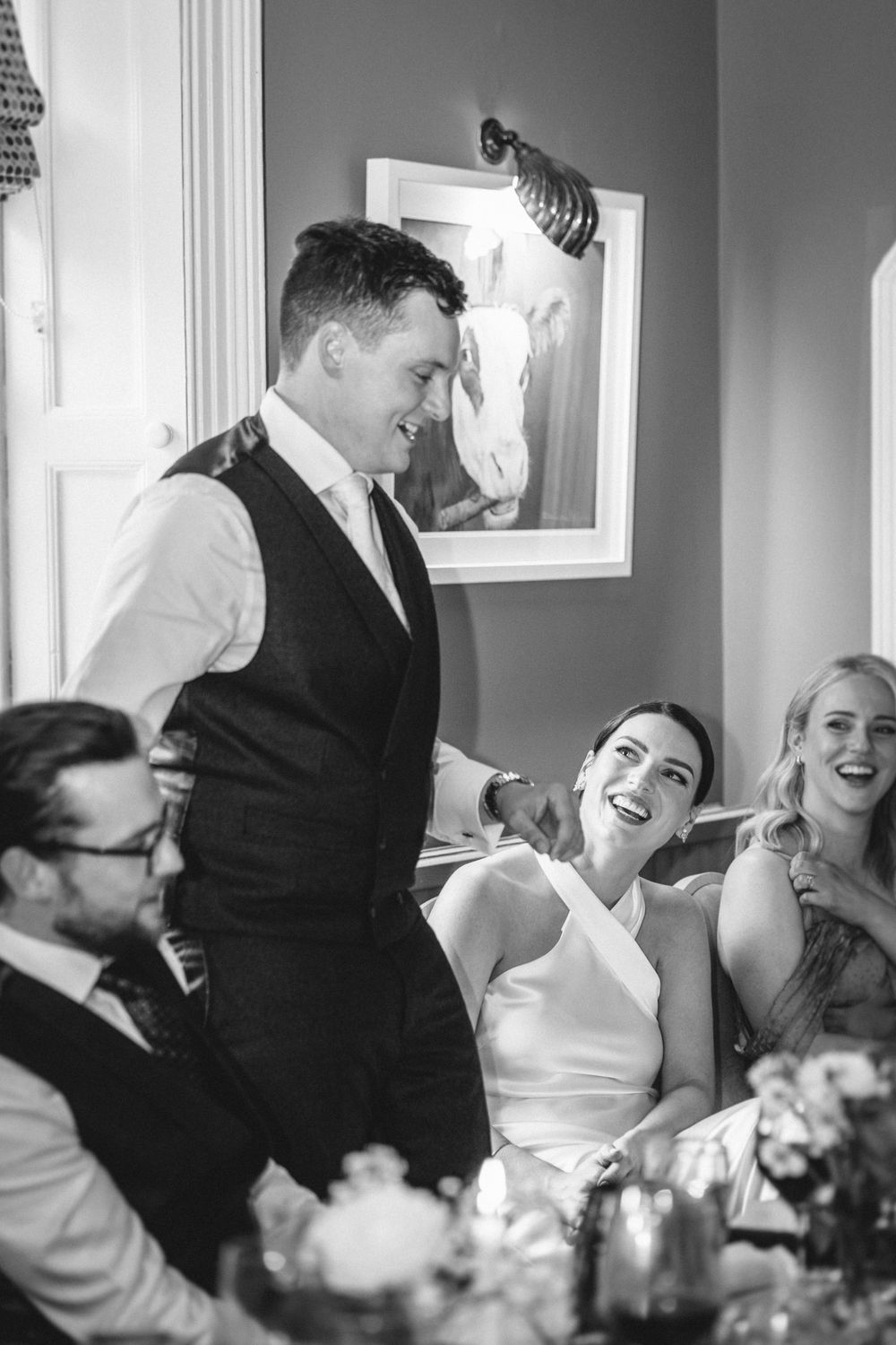 Candid moment of laughter during wedding reception speeches at an elegant indoor venue.