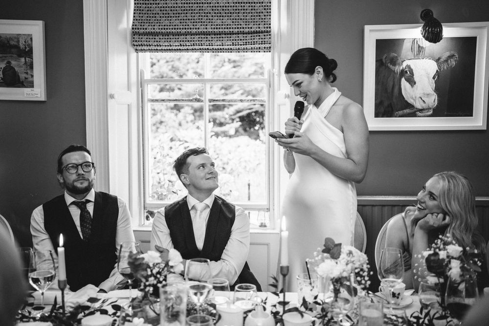 Black and white photo of wedding reception speeches with guests seated at decorated tables.