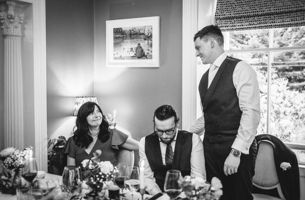 Black and white photo of wedding guests sharing a moment at an elegantly decorated reception table.