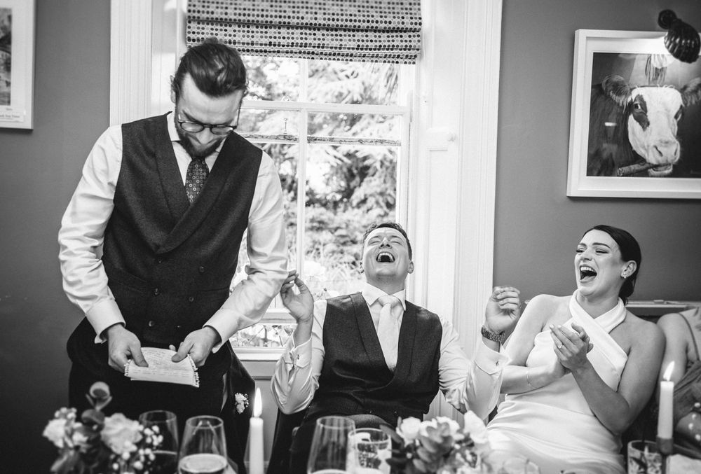 Candid black and white photo capturing laughter during wedding reception speeches.