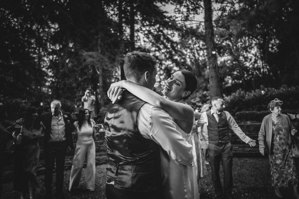 A wedding couple shares a dramatic dip dance move outdoors surrounded by guests in black and white.
