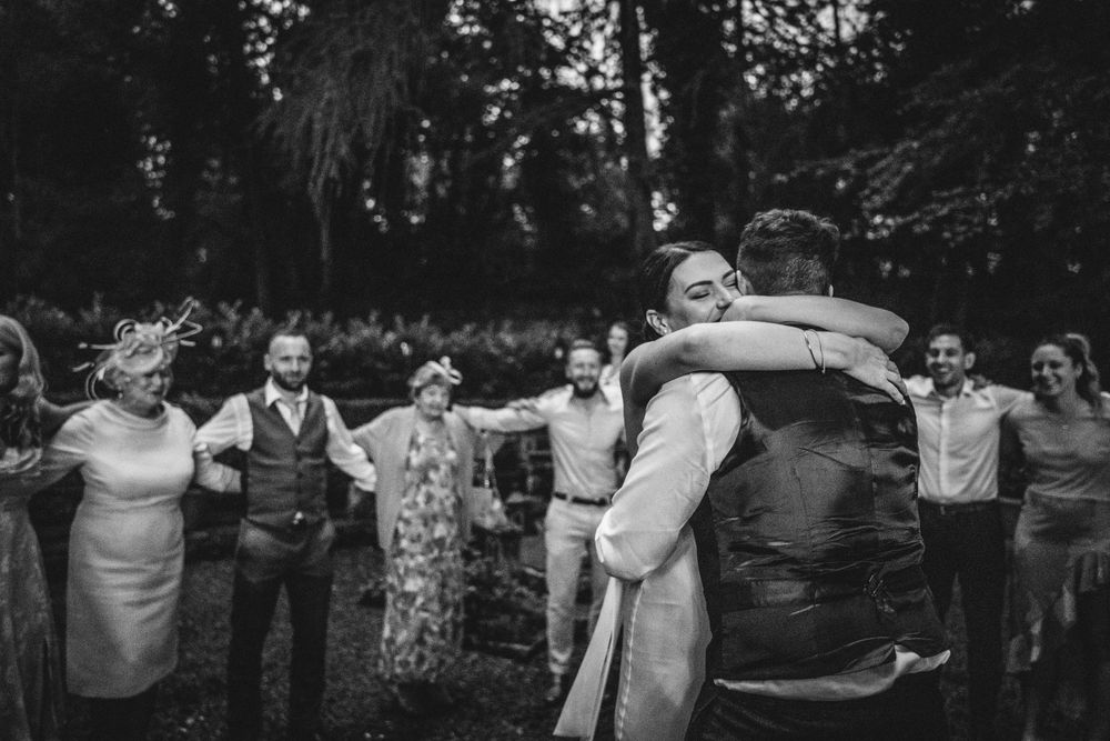 Wedding celebration dance in a garden setting with guests forming a circle around the dancing couple.