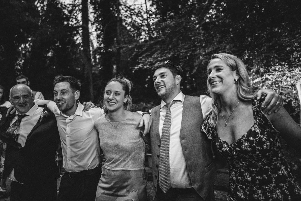 Wedding guests laugh and celebrate together outdoors in a candid black and white moment.