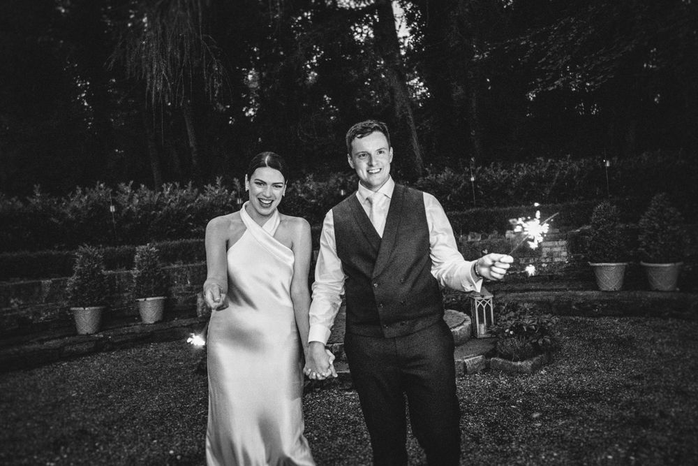 Black and white photo of couple holding sparklers during evening wedding celebration.