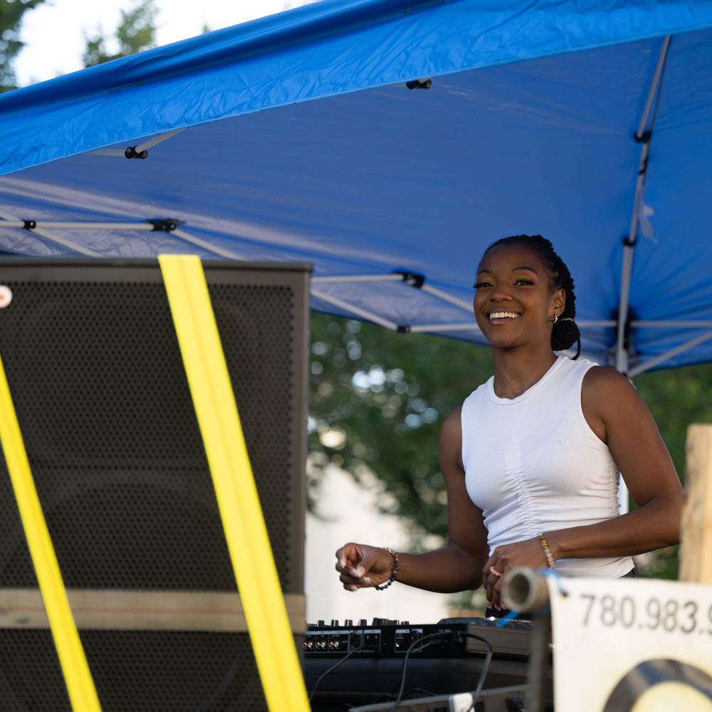 DJ performs at an outdoor event under a blue tent with professional audio equipment and speakers.