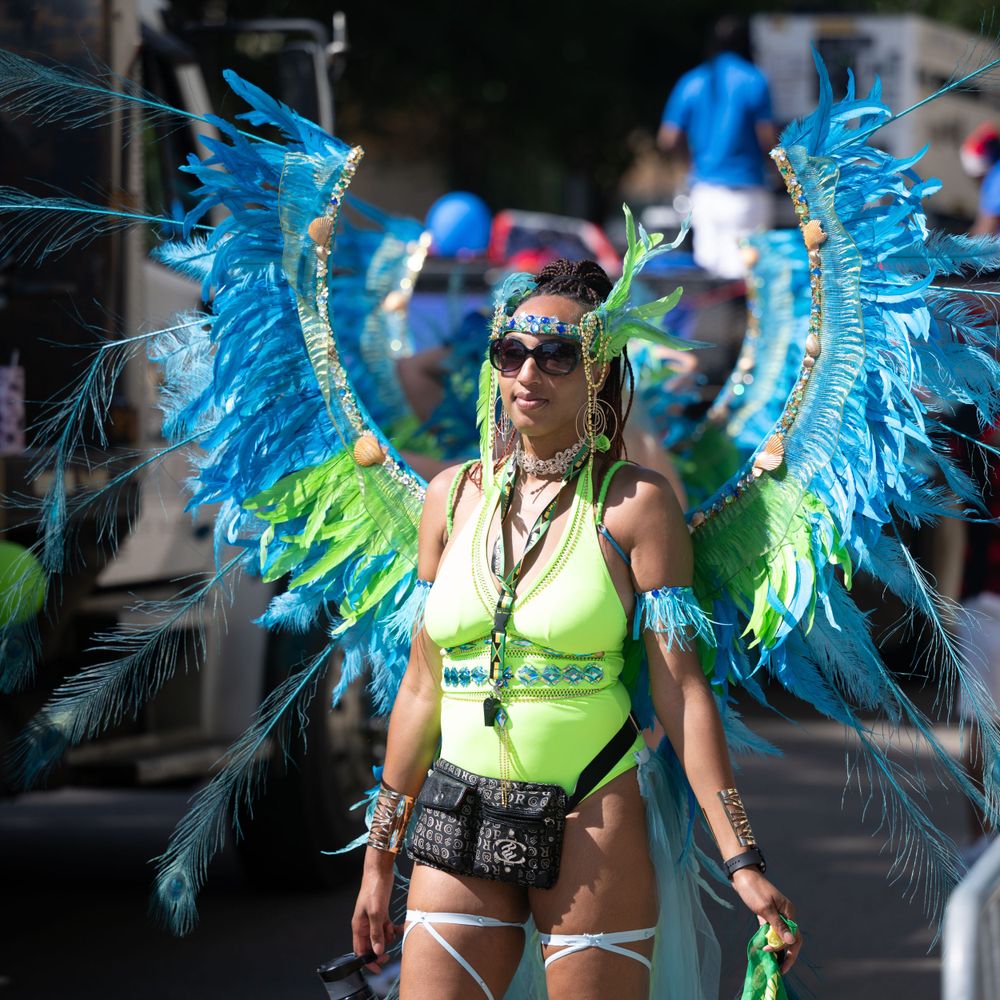 Carnival dancer in neon yellow top and vibrant blue feathered wings performs during a street festival celebration.
