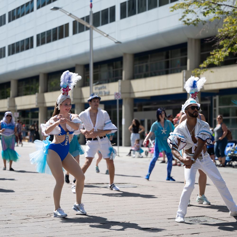 Capoeira performers practicing martial arts moves in sequence on an outdoor plaza in white and blue uniforms.