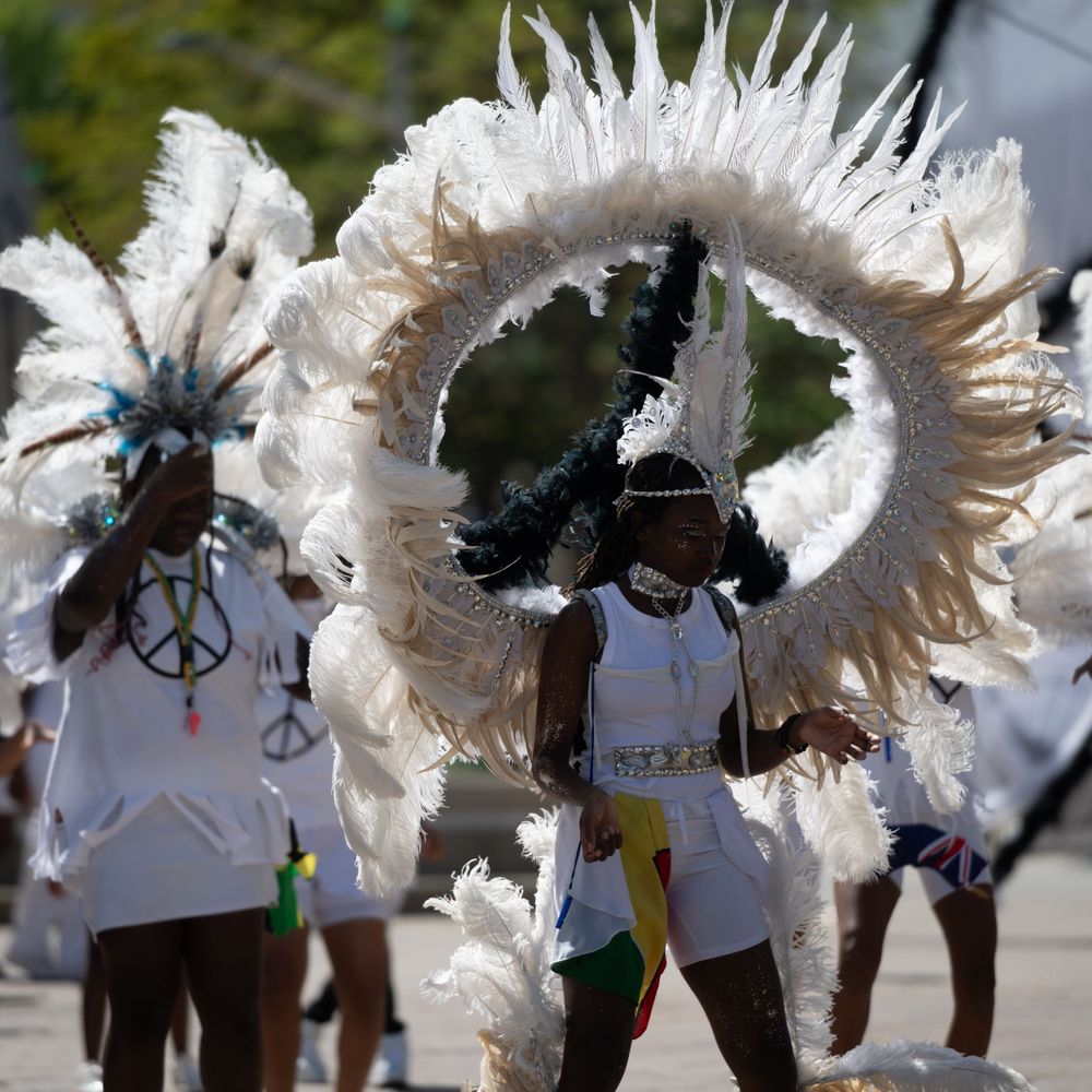 Performers in white outfits with large feathered wings dance during a parade or festival performance.