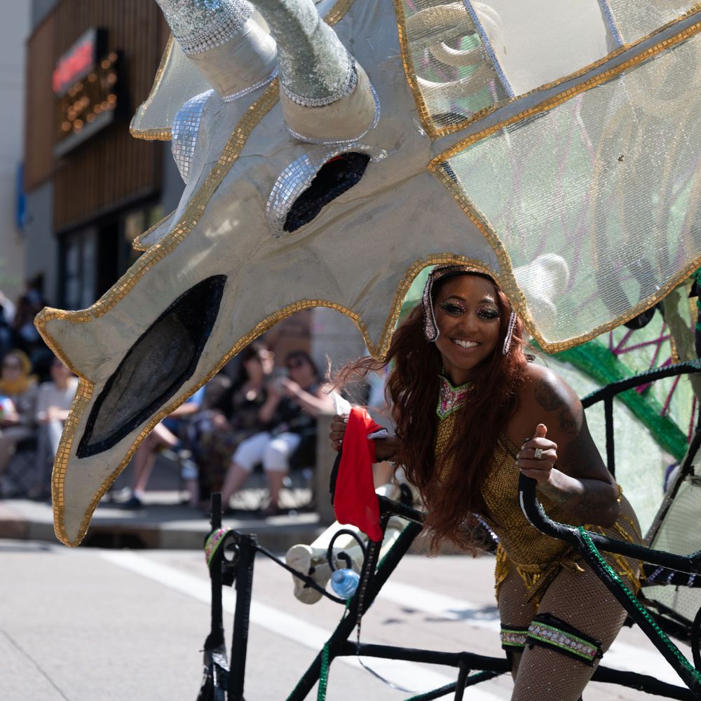 A participant rides a decorative bicycle with large artistic elements during a parade or festival event.