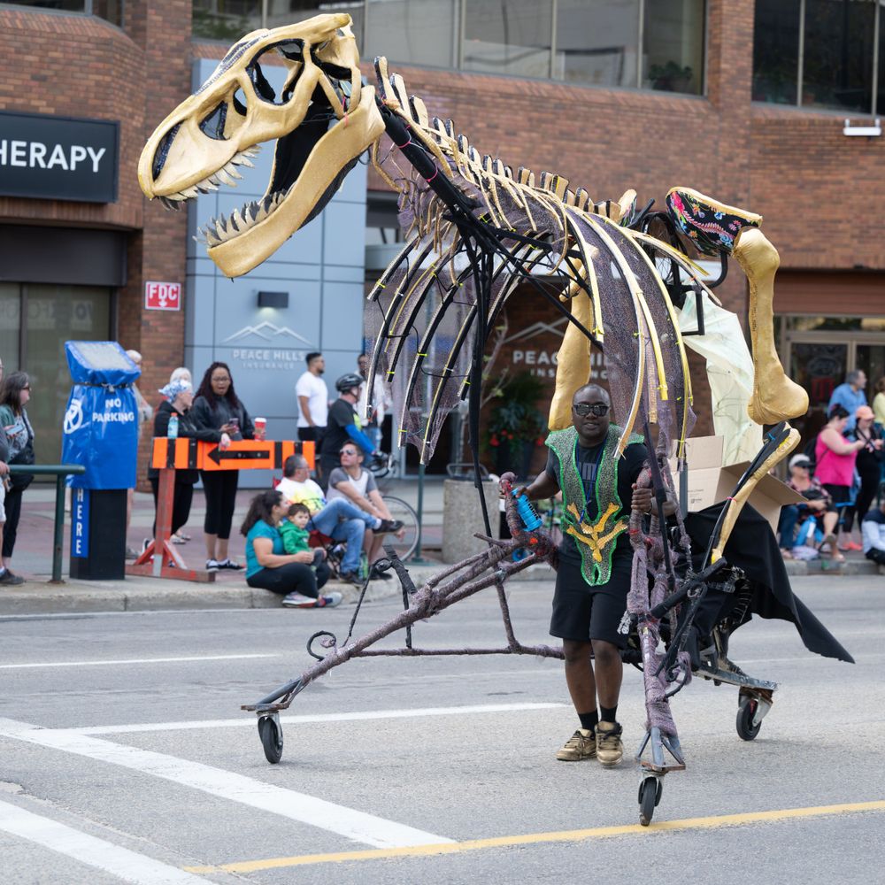 Life-sized dinosaur skeleton replicas displayed outdoors in an urban setting with brick buildings in the background.