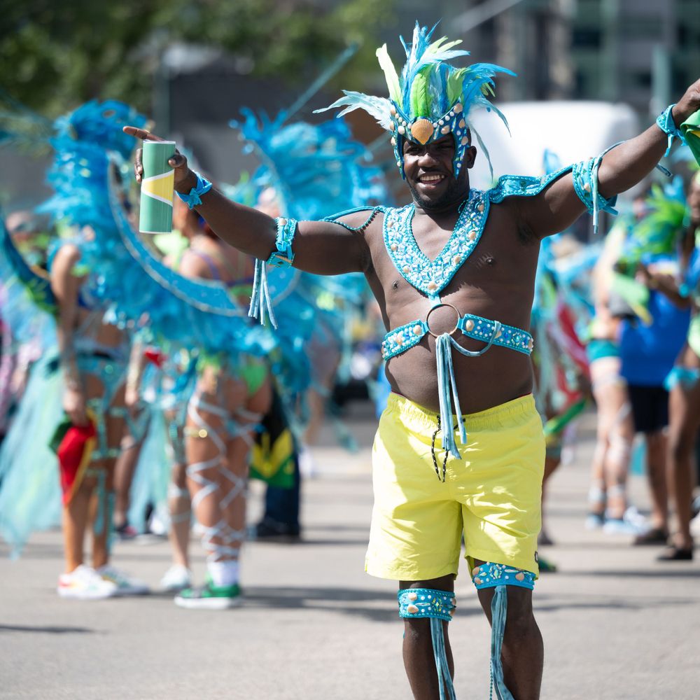 Carnival dancers in bright turquoise feathered costumes and yellow shorts perform during a festive parade celebration.