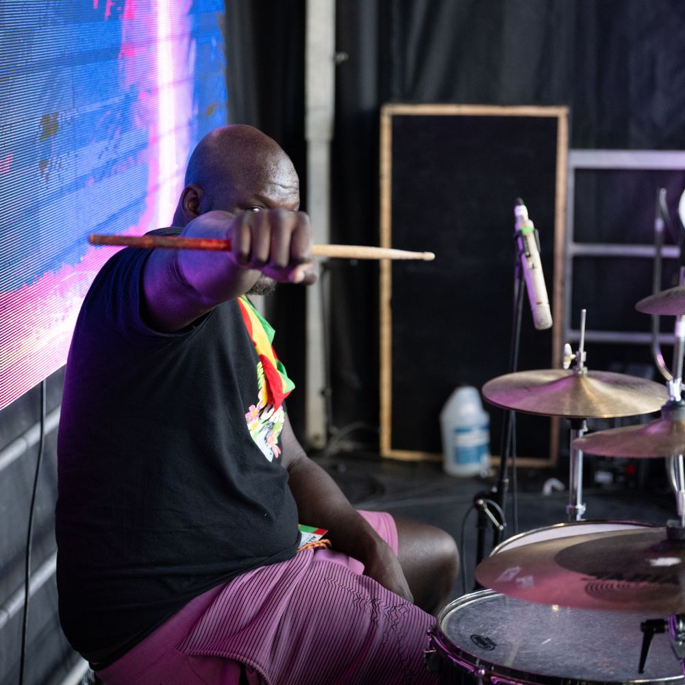 Drummer performing on stage with dramatic blue lighting and cymbals in a dark concert venue.