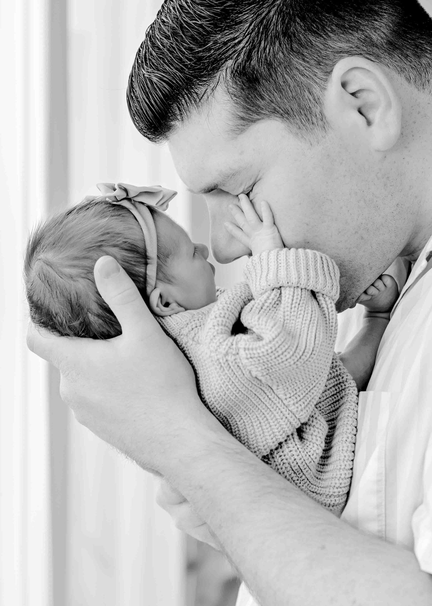 Intimate black and white portrait of a parent sharing a close moment with their newborn baby.