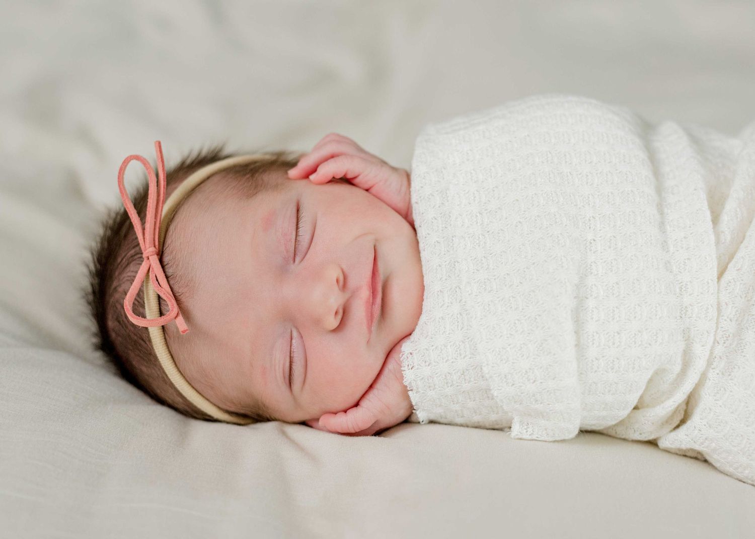 Sleeping newborn wrapped in white with a delicate pink bow headband.