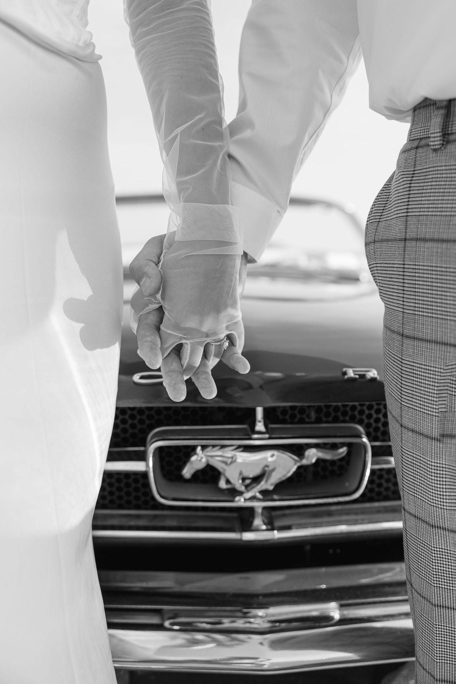 Close-up of clasped hands in front of a classic Ford Mustang emblem.