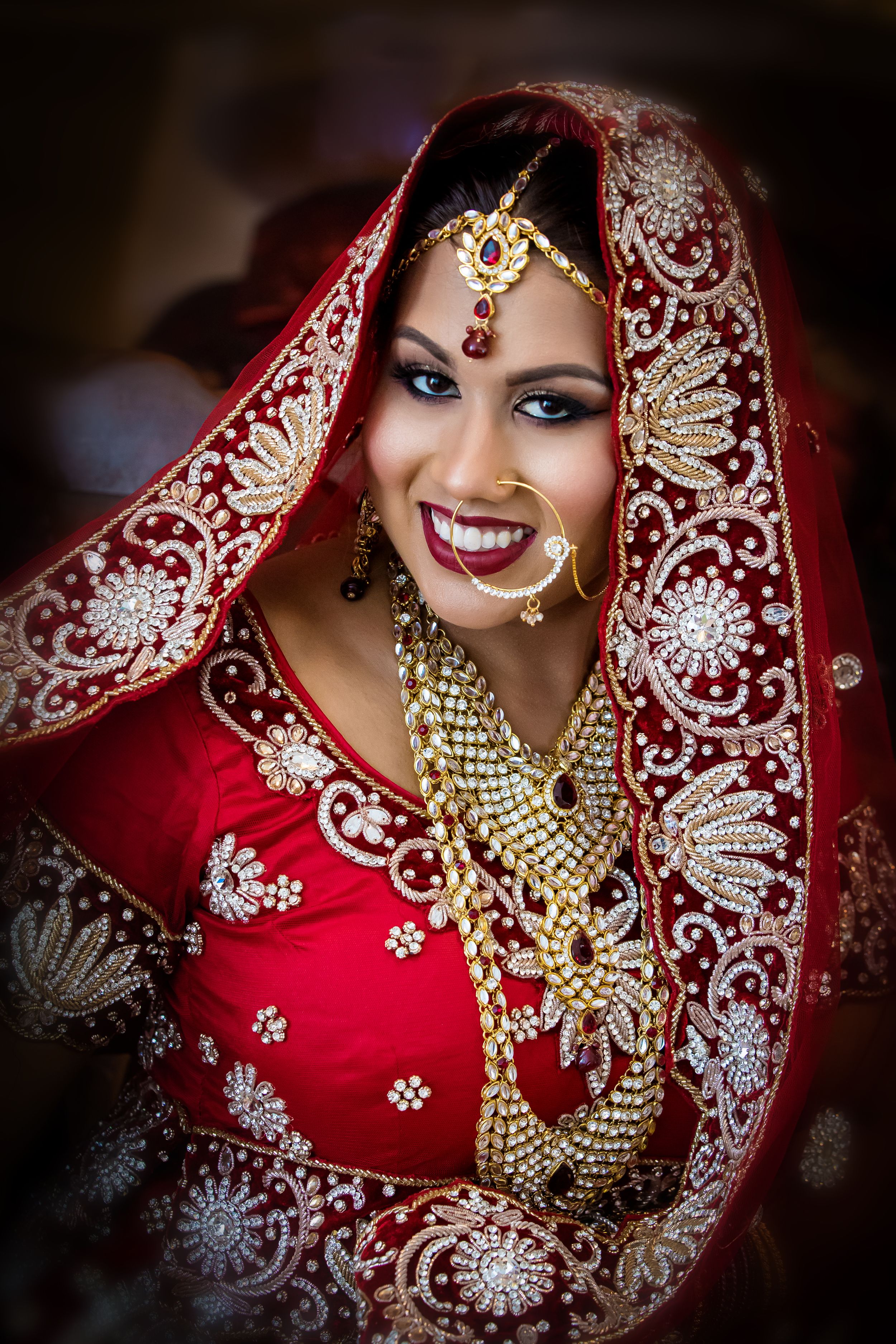 Detailed shot of elaborate Indian bridal jewelry and embroidered red wedding attire.