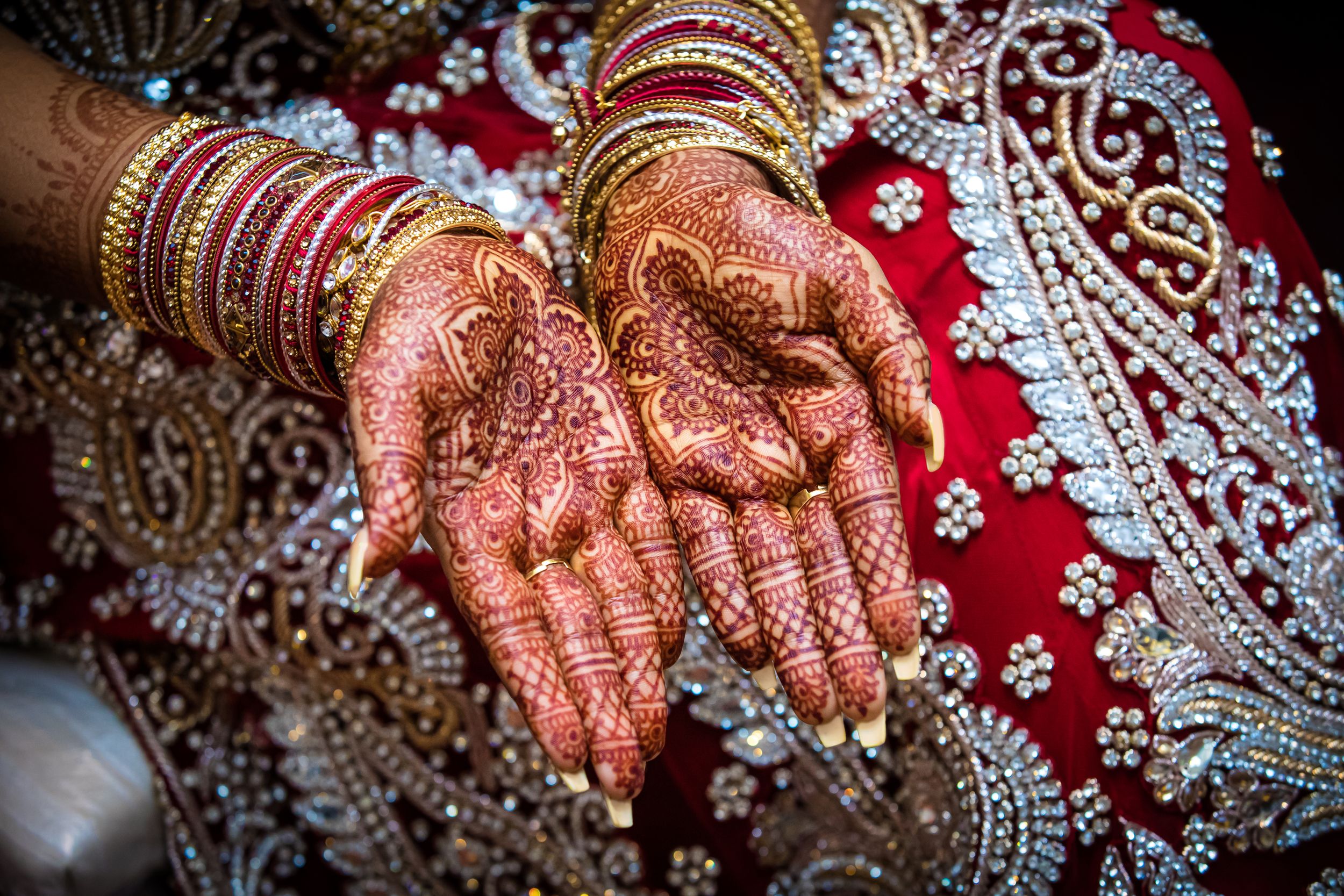 Close-up of henna-adorned hands with traditional bangles against red fabric.