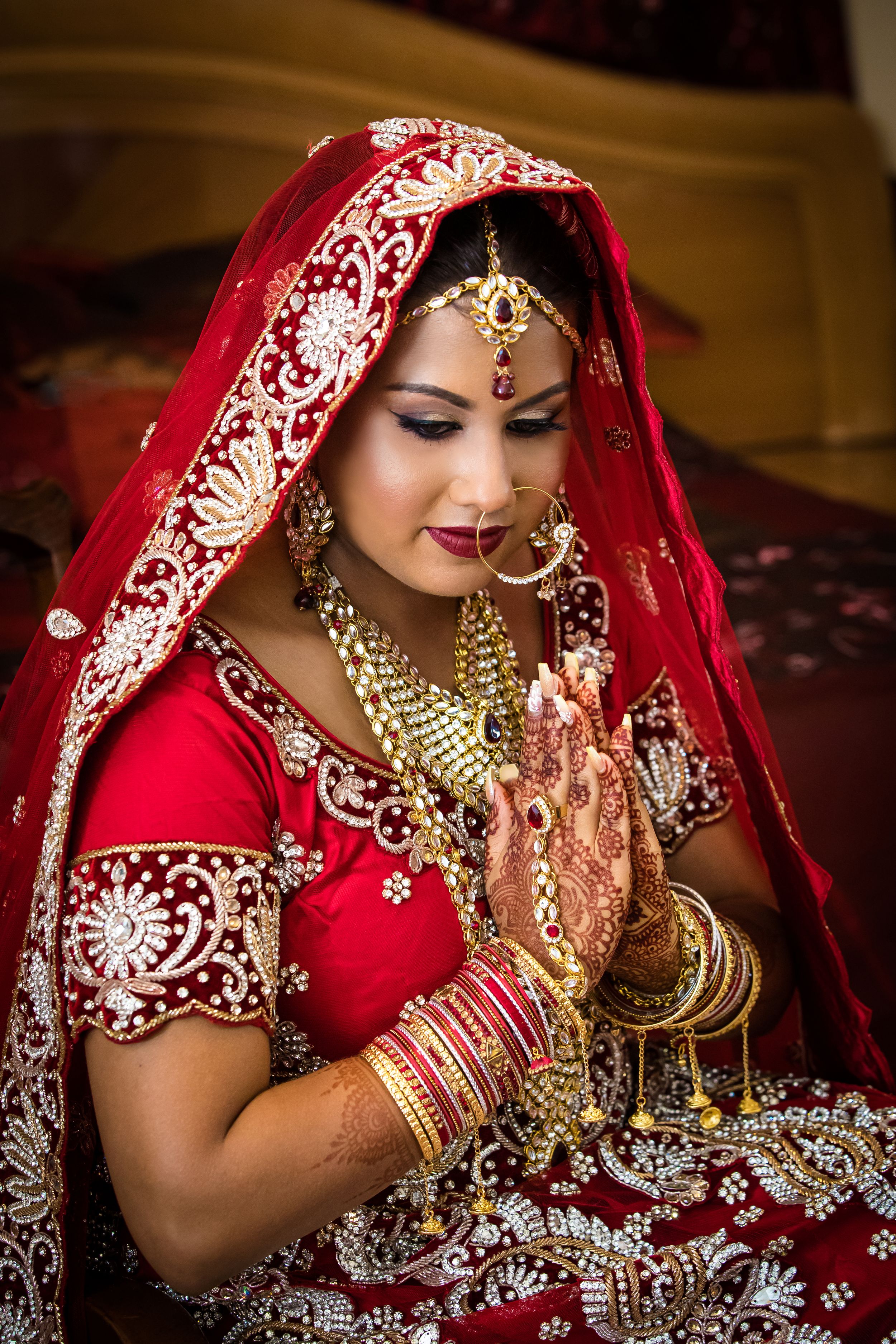 Traditional Indian bridal ensemble with gold jewelry and embroidered red fabric details.