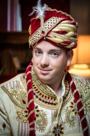 Traditional Indian groom wearing an embellished cream sherwani with red and gold turban.
