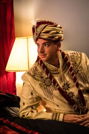 Groom in traditional Indian attire relaxing on couch with warm lighting.